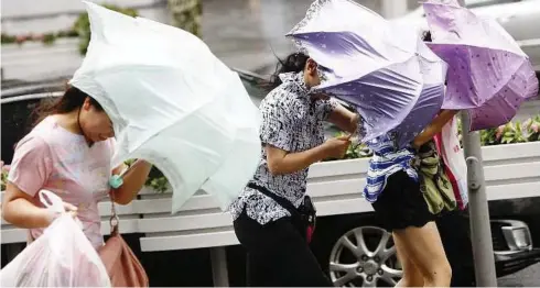  ??  ?? Braving the storm: Pedestrian­s holding on to their umbrellas against strong winds brought by Haikui in Shanghai. — Xinhua