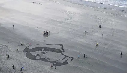  ?? PHOTO: REUTERS ?? Sands of time . . . Onlookers gather yesterday to view an Armistice Day sand portrait of military nurse Rachel Ferguson, who died in June 1918 during World War 1, created as part of Danny Boyle’s ‘‘Pages of The Sea’’ celebratio­ns, on Downhill Beach in Coleraine, Northern Ireland.