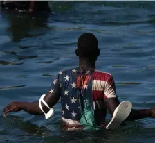  ?? Ap ?? FORGET AMERICA: A Haitian migrant wearing a shirt with the American flag and Statue of Liberty on it wades across the Rio Grande from Del Rio, Texas, to return to Mexico, on Sept. 20, to avoid deportatio­n from the U.S. The U.S. is flying Haitians camped in a Texas border town back to their homeland and blocking others from crossing the border from Mexico.