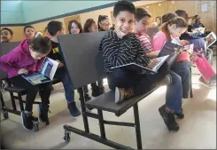  ?? Photo by Ernest A. Brown ?? Second and third graders, including from left, Jamal Loaza, Camren Vanasse and Brooke Allaire, at Globe Park School wasted no time in diving into new books they received from Mayor Lisa Baldelli-Hunt and members of the Woonsocket police and fire...