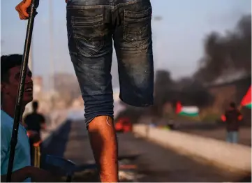  ??  ?? A Palestinia­n amputee protester stands with a crutch on a concrete barricade while smoke plumes from burning tires billow in the background, during clashes with Israeli forces following a demonstrat­ion at the Erez border crossing with Israel in the northern Gaza Strip. — AFP photo