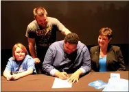  ?? Photo by Steve Huckriede ?? Grayson Brown, a 2018 graduate of Gravette High School, signs to participat­e in theater at Southern Arkansas University in Magnolia. Brown received a full performing arts scholarshi­p from SAU. Looking on are Brown’s sister, Grace Finley; his mother, Heather Finley; and Ian Galloway (standing), his drama teacher at Gravette.