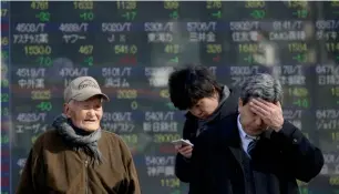  ?? — AP ?? People stand in front of an electronic stock board of a securities firm in Tokyo on Monday. Analysts say global indices have started on the back foot after US President Donald Trump announced one of his most radical policies yet in the form of a travel...