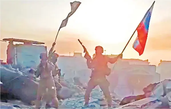  ?? ?? The cost of the war Wagner group mercenarie­s celebrate by raising Russian flags in the sunset amid the ruins of a devastated city