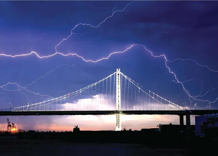  ??  ?? Lightning forks over the San Francisco-Oakland Bay Bridge as a storm passes over Oakland, California on Sunday. Numerous lightning strikes early Sunday sparked bush fires throughout the region. Photo: AP