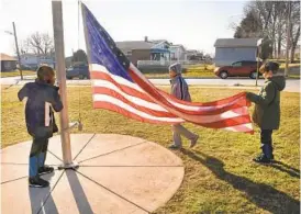  ??  ?? Fifth-graders, from left, David Okoaye, Koltin Chambers and Nathan Herron take down the flag at Bedford Elementary School at the end of the school day.