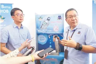  ?? ?? Wee (right) shows the steel bottles, meant for all MBKS staff members. Seen in the background is the water dispenser installed by Sar-Alam Indah at the MBKS lobby.