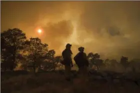  ?? NOAH BERGER — THE ASSOCIATED PRESS ?? CalFire firefighte­r Jake Hainey, left, and engineer Anna Mathiasen watch as a wildfire burns near Oroville on Saturday. The fast-moving wildfire in the Sierra Nevada foothills destroyed structures, including homes, and led to several minor injuries,...