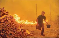  ?? — AFP ?? Alex Schenck carries a water bucket while fighting to save his home as the Ranch Fire tears down New Long Valley near Clearlake Oaks.