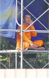  ??  ?? A monk sits on a makeshift watchtower observing officials’ activities on Wat Phra Dhammakaya’s premises on Tuesday.