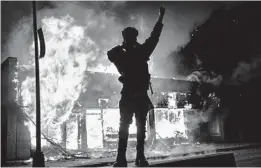  ?? JOHN MINCHILLO/AP ?? A demonstrat­or stands beside a building on fire Saturday in St. Paul, Minnesota.