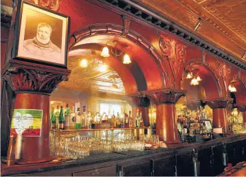  ?? KATHERINE RODEGHIER/CHICAGO TRIBUNE ?? A portrait of Ernest Hemingway looks down from the mahogany bar at City Park Grill in Petoskey, Michigan. Hemingway enjoyed playing pool at the saloon and watching boxing matches in the nearby park.