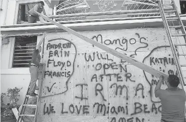  ?? AP Photo/Marta Lavandier ?? Workers shutter Mango’s Tropical Cafe on Thursday in Miami Beach, Fla. The National Hurricane Center issued a hurricane watch for the Florida Keys and parts of South Florida, the first of perhaps many watches and warnings along the Southeaste­rn coast...