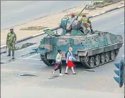  ??  ?? Young women walk past an armoured vehicle stationed by an intersecti­on as Zimbabwe soldiers regulate traffic in Harare.