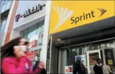  ?? THE ASSOCIATED PRESS ?? A woman using a cell phone walks past T-Mobile and Sprint stores in New York. T-Mobile and Sprint are trying again to combine in a deal that would reshape the U.S. wireless landscape, the companies announced Sunday.