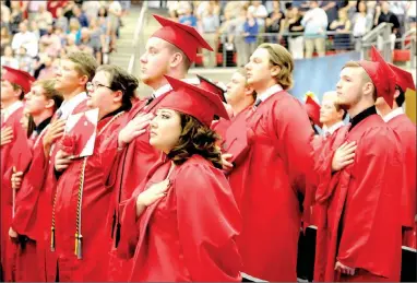  ??  ?? Farmington graduates salute the Flag of the United States of America while the Crimson Select Ensemble and the Farmington High School band perform the National Anthem during graduation ceremonies at Cardinal Arena.