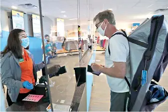  ?? AP Photo/LM Otero ?? ■ Amid concerns of the spread of COVID-19, a cashier and customer are separated by plexiglass May 29 at the city owned waterpark in Grand Prairie, Texas. Water parks in Texas were allowed to reopen today.