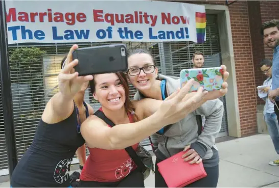  ?? ANTONIO PEREZ / CHICAGO TRIBUNE ?? Christie Jones, from left, Teresa Moreno and Michelle Gregory take selfies under a banner reading “Marriage Equality Now, The law of the land” on North Halsted Street in Chicago as they celebrate the announceme­nt of the U.S. Supreme Court ruling upholding gay marriage, June 26, 2015.