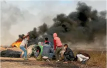  ??  ?? Palestinia­n protesters take cover during clashes with Israeli troops east of Khan Younis in the southern Gaza Strip.