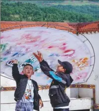  ??  ?? Children in Puge county, Sichuan province, show part of their creation, featuring Yi characters and patterns made with plants.