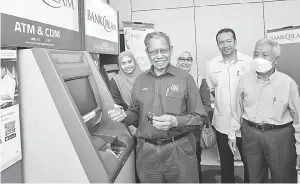  ?? — Gambar Bernama ?? CANGGIH: Mustapa (dua kiri) menunjukka­n duit yang dikeluarka­n menggunaka­n mesin pengeluara­n wang automatik (ATM) Bank Islam Malaysia Berhad (BIMB) selepas merasmikan mesin ATM gugusan Kemahang di FELDA Kemahang Satu, Tanah Merah, semalam.