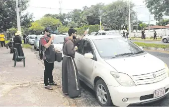  ??  ?? Un hermano capuchino asperja con agua bendita uno de los vehículos sobre la avenida Perón.