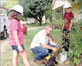  ?? LYNN KUTTER ENTERPRISE-LEADER ?? Kris Phillips, safety director with PG Telco, works on installing a wireless internet connection to Historic Cane Hill Museum. Mariah Huffmaster, left, and Trey Reed, two students with the EAST class at Lincoln Middle School, are working on a project...