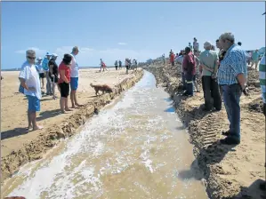  ??  ?? CONTENTIOU­S ISSUE: Residents and visitors of Aston Bay and Paradise Beach watch the water flowing into the sea after a breach at the causeway to alleviate the frequent flooding
