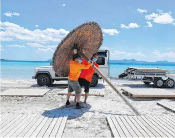  ?? FOTO: CLARA MARGAIS/DPA ?? Männer stellen Sonnenschi­rme am Strand Alcudia im Norden von Mallorca auf. Spanien will seine Grenzen für Bürger aus Schengenst­aaten ab dem 21. Juni öffnen. Doch völlig unbeschwer­t wird das Reisen künftig nicht.
G