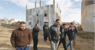  ?? (Muhammad Hamed/Reuters) ?? PEOPLE WALK past a building that was the site of clashes between Jordanian police and Islamist gunmen in the village of Garifla, in Karak, yesterday.