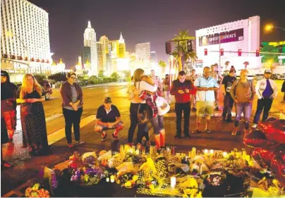  ?? PHOTO BY ERIC THAYER/THE NEW YORK TIMES ?? People gather at a makeshift memorial on the Las Vegas Strip. A lone gunman, identified as Stephen Paddock, fired down from a 32nd-floor suite in the Mandalay Bay Resort and Casino upon a crowded country music festival on Sunday night, killing at least...
