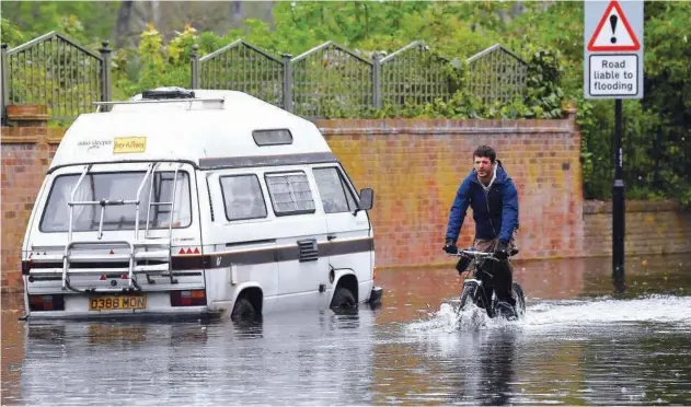  ?? Reuters ?? ↑ A man cycles through a flooded road in London, Britain, on Wednesday.