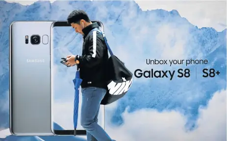  ?? /Reuters ?? Cloud nine: A man using his cellphone walks past an advertisem­ent promoting a Samsung Galaxy S8 smartphone at a shop in Seoul. Huge sales of the new smartphone and demand for its memory chips were behind the jump in operating profit in the April-to-June period.