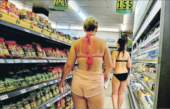  ?? ÀLEX GARCIA ?? Contra la normativa. Dos turistas vestidas únicamente con el bikini comprando en un supermerca­do del barrio