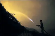  ?? ARMANDO FRANCA/THE ASSOCIATED PRESS ?? A volunteer uses a water hose to fight a wild fire raging near houses in the outskirts of Obidos, Portugal.