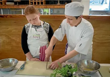  ?? GRANT MATTHEW/STUFF ?? Chef Helen Flitcroft from Cook Learn Love shows Ashley Lewis, 10, the correct way to chop herbs.
