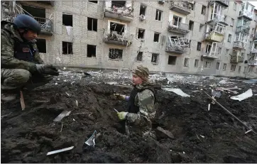  ?? PHOTOS BY ANDRII MARIENKO – THE ASSOCIATED PRESS ?? Police officers inspect a crater in front of a damaged residentia­l building hit by a Russian strike in Kharkiv, Ukraine, Wednesday.