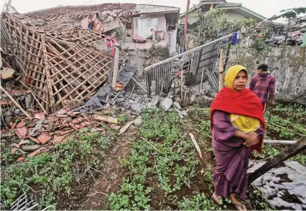  ?? Associated Press ?? A woman walks past one of many homes damaged by a powerful earthquake in the town of Cianjur, West Java, Indonesia.