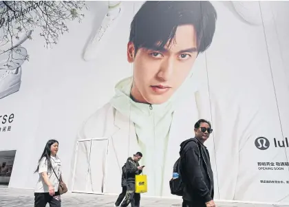  ?? AFP ?? People walk past a billboard showing Chinese race-car driver Zhou Guanyu at a shopping mall in Beijing yesterday.