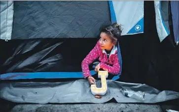  ?? Gary Coronado Los Angeles Times ?? SOFIA MERCEDES, 7, peeks out of her tent Tuesday at a Tijuana encampment set up this week by Central American migrants waiting to be let through a U.S. port of entry. The last group entered about 9 a.m. Friday.