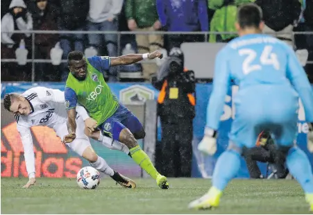  ??  ?? Whitecaps defender Jake Nerwinski, left, tugs on the jersey of Sounders’ Nouhou in front of Vancouver goalkeeper Stefan Marinovic.