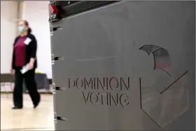  ?? (File Photo/AP/Ben Gray) ?? A worker passes a Dominion Voting ballot scanner Jan. 4, 2021, while setting up a polling location at an elementary school in Gwinnett County, Ga., outside of Atlanta. Stories circulatin­g online incorrectl­y claim election technology firm Dominion Voting Systems lost its lawsuits against attorney Sidney Powell and former President Donald Trump’s personal lawyer Rudy Giuliani.