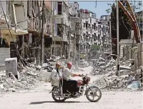  ?? AFP PIC ?? Two men riding a motorbike along a destroyed street in Douma on the outskirts of Damascus, Syria, on Monday.