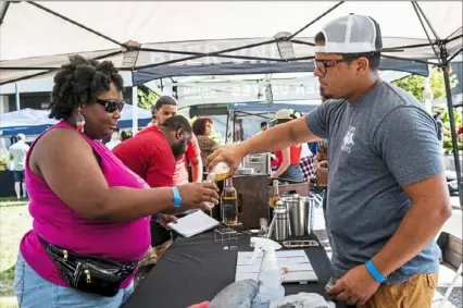  ?? Michael M. Santiago/Post-Gazette ?? Ashley Gilyard, left, of Temple Hills, Md., holds a cup as Jonathan Ortiz, of Baltimore, the co-owner and master distiller at Rams & Parrots Whiskey, pours her some whiskey during the Fresh Fest black beer festival Saturday at Nova Place on the North Side.