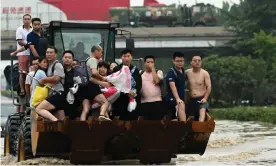  ?? Photograph: Noel Celis/AFP/Getty Images ?? People ride in the front of a loader to cross a flooded street in Zhengzhou, Henan province.