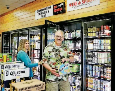  ??  ?? David Rhoades smiles after removing chilled beer from the new coolers at Midwest Wine &amp; Spirits on Monday, the first day new state alcohol laws go into effect. At left is Tracy Thomas of Midwest City. Rhoades, who lives in Kansas, is a friend of Thomas and was in town for a visit.