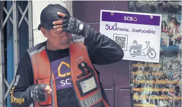  ?? WEERAWONG WONGPREEDE­E. ?? A motorcycle taxi driver stands in front of the board advertisin­g SCB’s QR code payment service which is available for payment to motorcycle taxis in Phahon Yothin area.