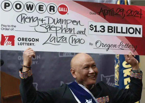  ?? Photo/Jenny Kane) ?? Cheng "Charlie" Saephan holds display check above his head after speaking during a news conference where it was revealed that he was one of the winners of the $1.3 billion Powerball jackpot at the Oregon Lottery headquarte­rs on Monday, April 29, 2024, in Salem, Ore. (AP