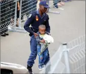  ?? PICTURE: REUTERS/AFRICAN NEWS AGENCY (ANA) ?? A police officer carries a boy holding flowers outside the house of Madikizela-Mandela in Orlando West, Soweto, yesterday.