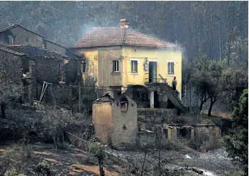  ?? MIGUEL RIOPA/GETTY IMAGES ?? A man stands in the stairway of a house with smoke billowing from the roof in an area devastated by a wildfire in Canical, near Alvares in Portugal, on Sunday.